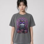 Woman wearing the anthracite Mahavatar Keanu Ultra Garment-Dyed Tee — Keanu in purple shades, paws together under a mandala halo